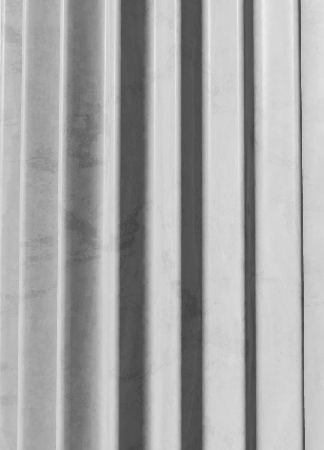 A monumental fluted stone pillar in pale weathered marble, lit softly from the side against a quiet gray gallery wall.