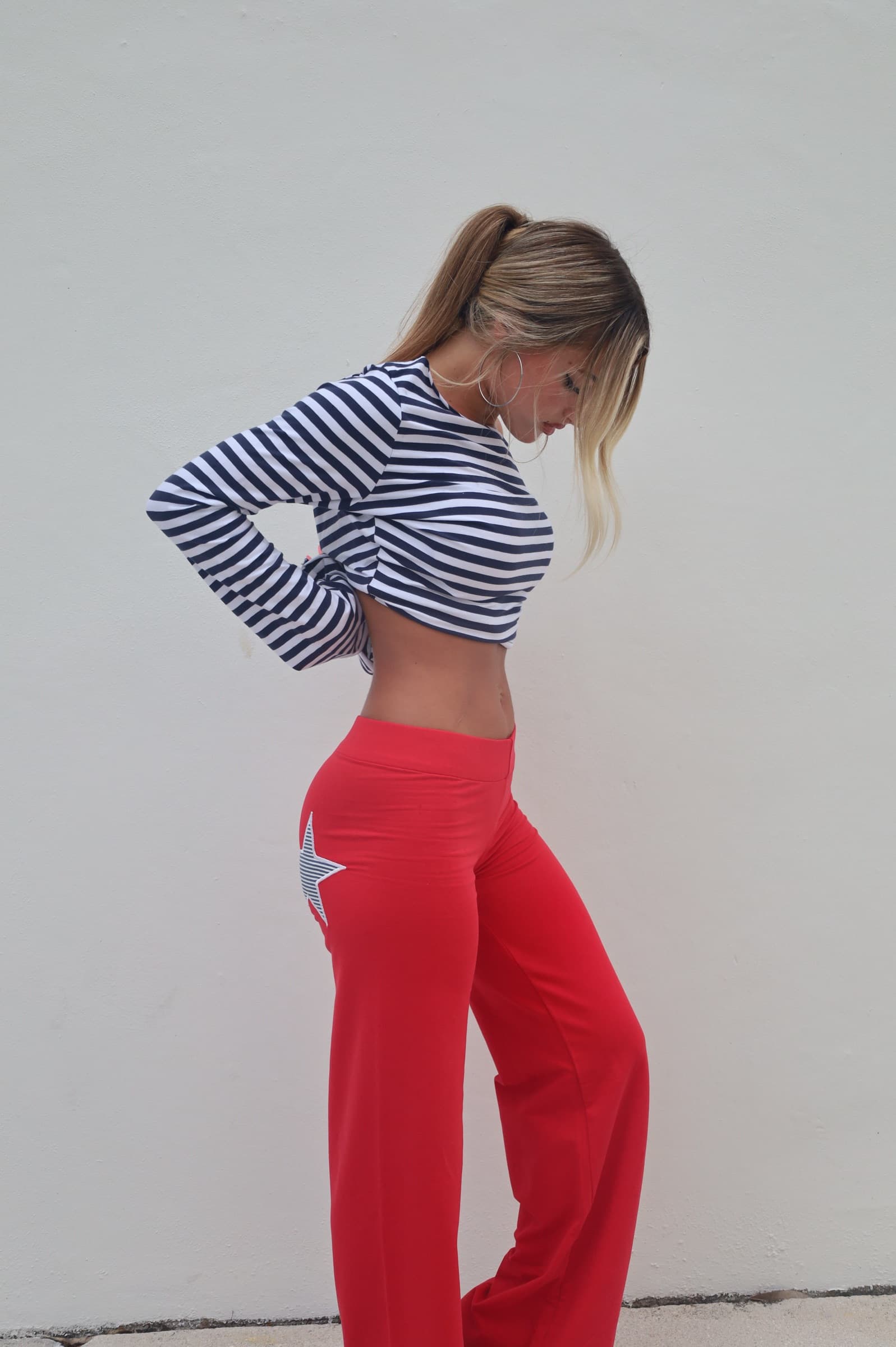 A woman in a navy-striped cropped top and red wide-leg pants with a striped star patch, against a white wall.